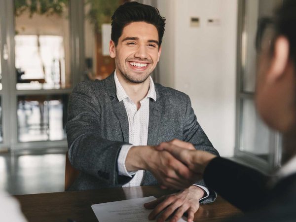 Two men sitting at a table, shaking hands and laughing.