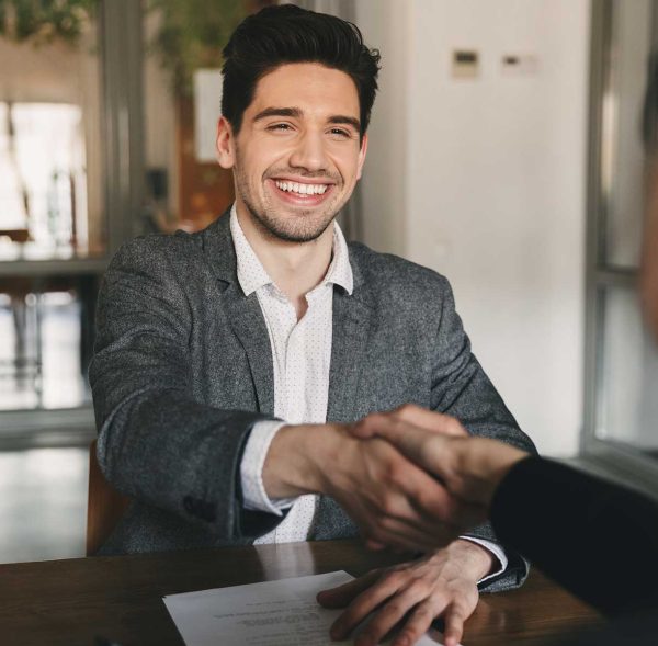 Two men sitting at a table, shaking hands and laughing.
