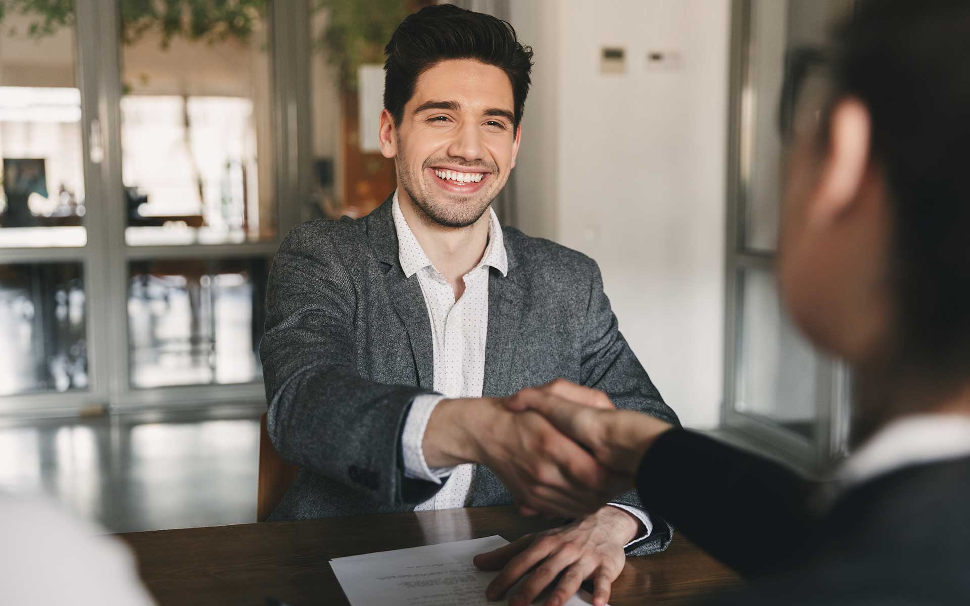 Two men sitting at a table, shaking hands and laughing.
