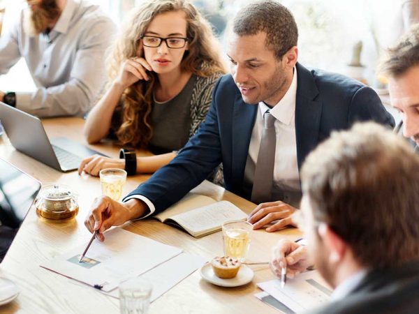 Group of people sitting together, discussing with a notebook.