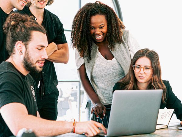Group of people gathered around a laptop, laughing