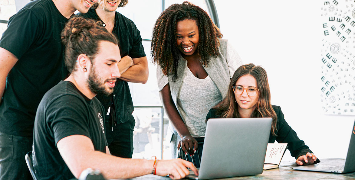 Group of people gathered around a laptop, laughing