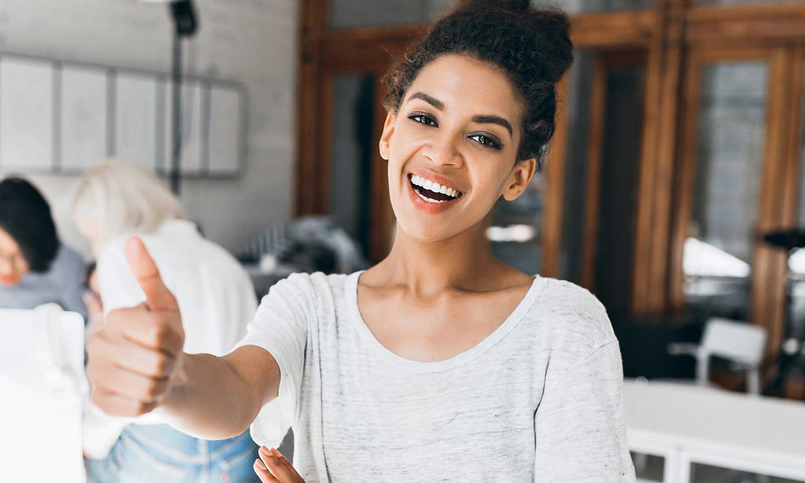 Woman smiling and giving a thumbs-up while speaking.