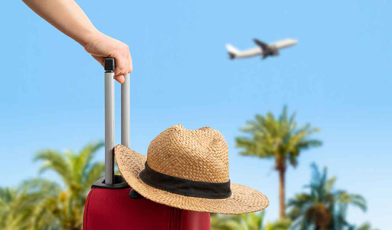 Person holding a travel bag with a hat on it and a plane in the background, symbolizing E-Travel Coverage