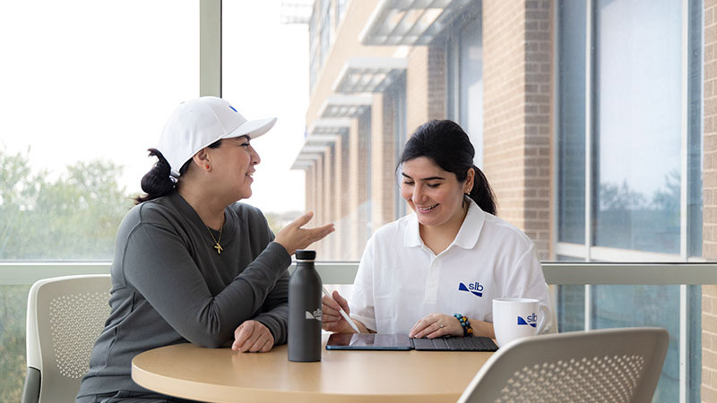 Two women talking and laughing, one using a tablet, representing SLB Flex Eligibility.