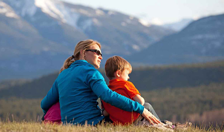 Woman sitting on a mountain holding her children, symbolizing SLB-dependents