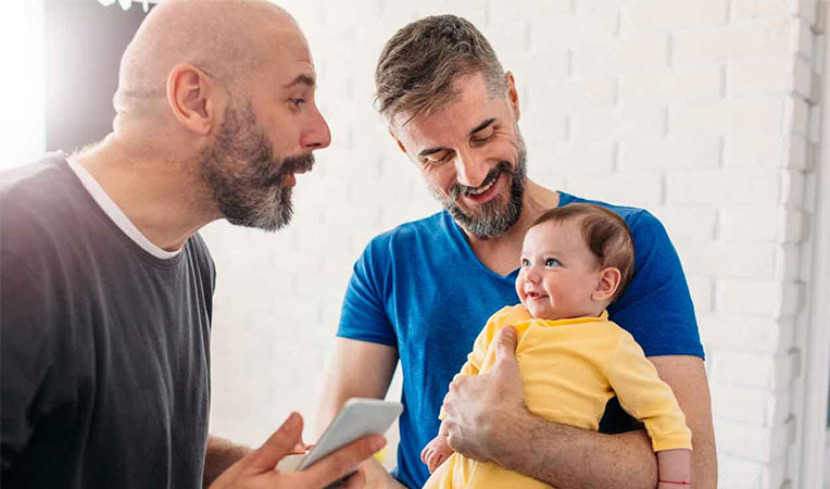 Two men happily talking to a child, one holding the child, symbolizing SLB Life Events