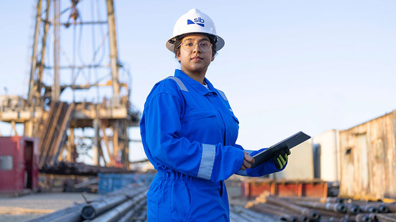 Woman in blue dress with white hat holding a tablet, representing SLB New Hire