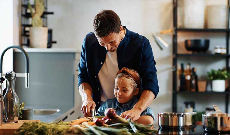 Man teaching child to cut vegetables, representing SLB Nutrition and Fitness
