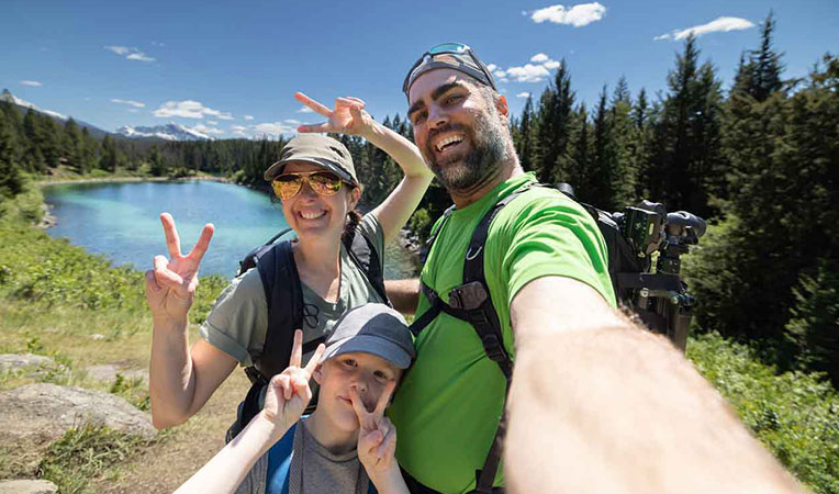 Smiling family couple with one child taking a selfie near a lake in the mountains