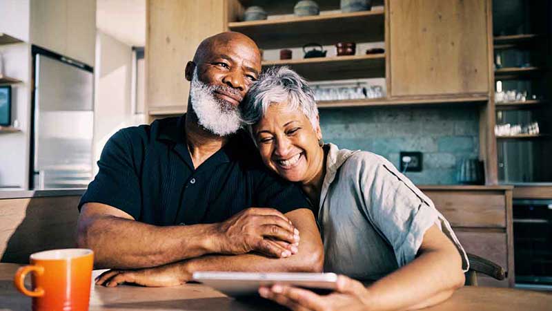 Happy elderly couple sitting together, woman resting her head on man's shoulder, symbolizing retirement savings plan