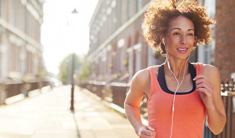 Woman running with headphones, symbolizing health and wellness.