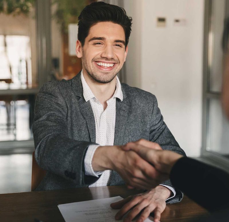 Two men sitting at a table, shaking hands and laughing.