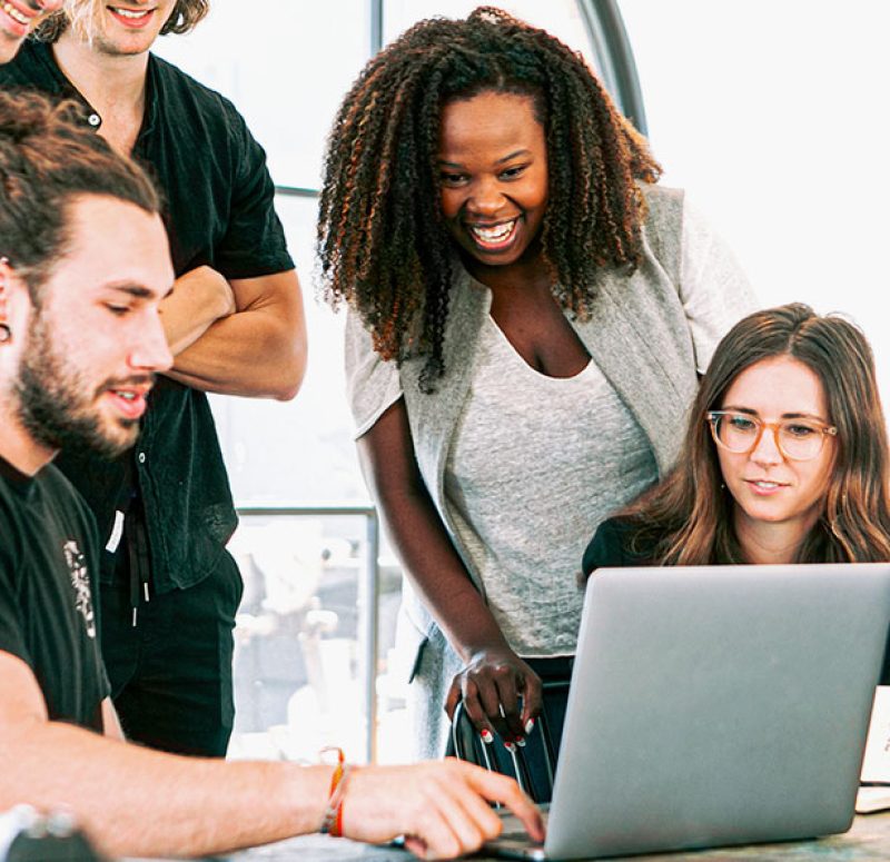 Group of people gathered around a laptop, laughing