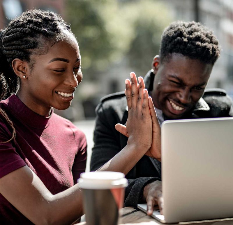 Man and woman using a laptop, smiling and giving a high five